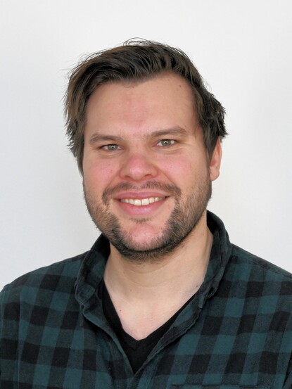 Mann der lächelt, mit kurzen Haaren und karriertem Hemd